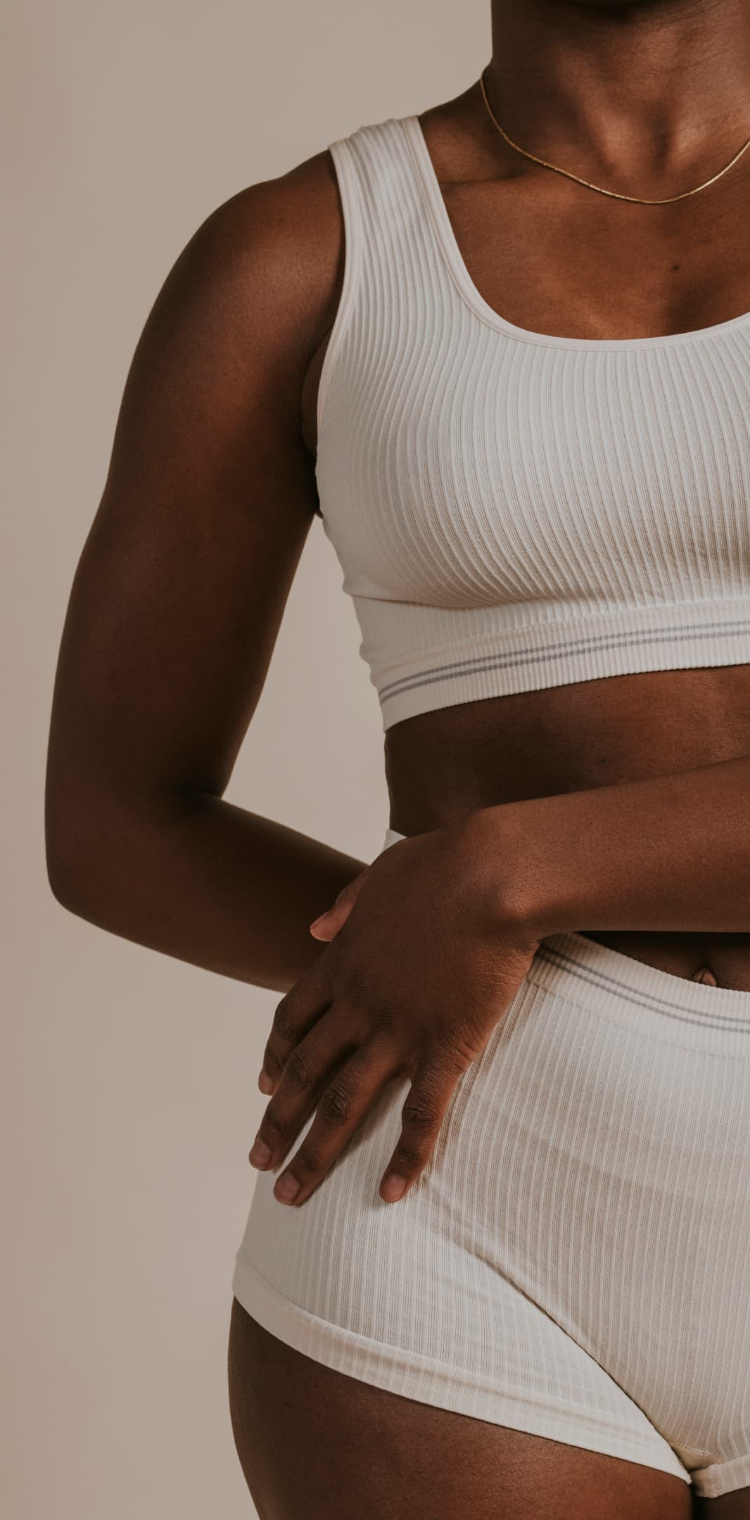 A person wearing a ribbed white tank top and shorts, with hands resting on their hips against a neutral background.